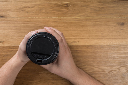 hand holding black paper coffee container on wooden background. Top view. Minimalismの写真素材