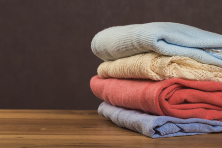 Bunch of knitted warm pastel color sweaters with different knitting patterns folded in stack on...
