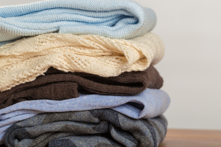 A pile of warm sweaters on a wooden table on a light background. Autumn and winter clothesの写真素材
