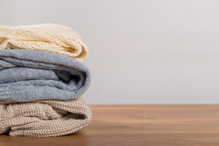 A pile of warm sweaters on a wooden table on a light background. Autumn and winter clothesの写真素材