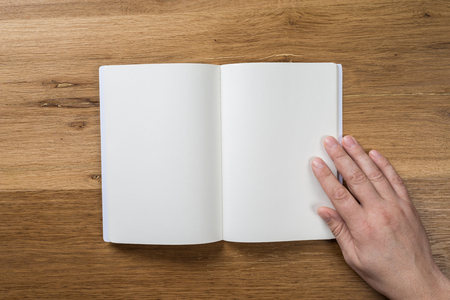 Hand holding white blank paper sheet mockup on wooden background. Arm in shirt hold clear brochure template mock up. Leaflet document surface design. Simple pure print display show. Reading contract agreement.の写真素材