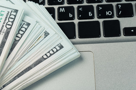 Closeup view of one hundred dollar banknotes lying on the laptop keyboard. Paying dollar for...