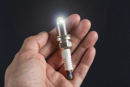 New spark plug in hand on a dark background
