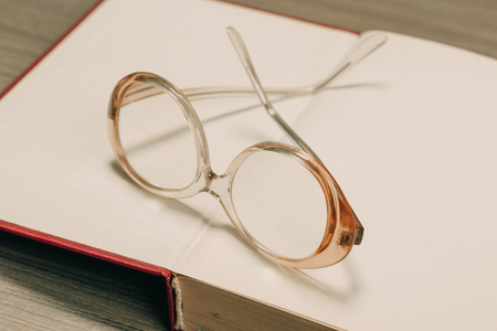 old book open on a wooden table with glassesの写真素材
