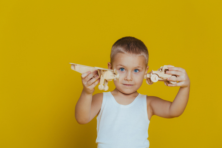 Portrait of an attractive boy in a white t-shirt playing wooden toys close-up, on a yellow backgroundの写真素材