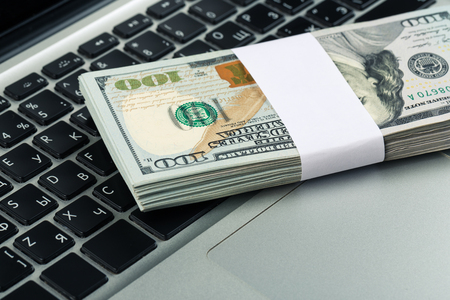 Closeup view of one hundred dollar banknotes lying on the laptop keyboard. Paying dollar for shopping and corruption concept.の写真素材