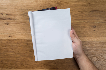 Hand holding white blank paper sheet mockup on wooden background. Arm in shirt hold clear brochure template mock up. Leaflet document surface design. Simple pure print display show. Reading contract agreement.の写真素材