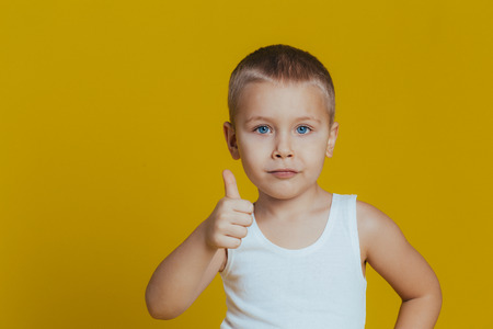 Cute boy on a yellow background raised his finger up and says ok and smilesの写真素材