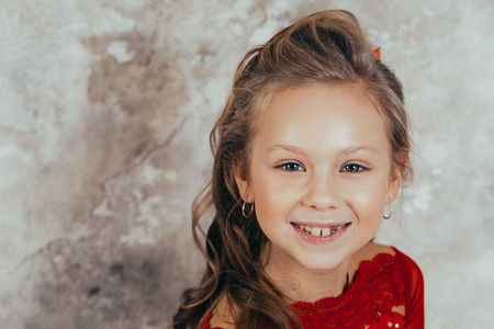 portrait of a smiling young girl in a red dress and with a beautiful hairstyle against the background of a grunge wallの写真素材