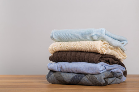 A pile of warm sweaters on a wooden table on a light background. Autumn and winter clothesの写真素材
