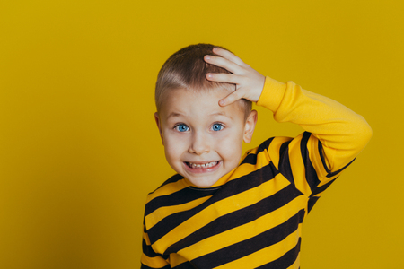 Portrait of an attractive thoughtful boy in a striped sweater holding a hand on his head close-up, on a yellow backgroundの写真素材