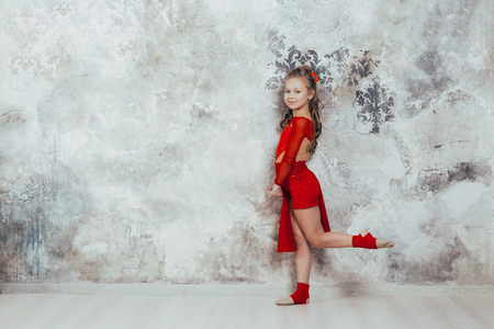 Girl gymnast in a red gymnastic swimsuit posing on studio background. practicing gymnasticの写真素材