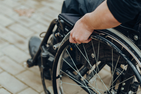 Close-up of male hand on wheel of wheelchair during walk in park. He holds his hands on the wheel.の写真素材