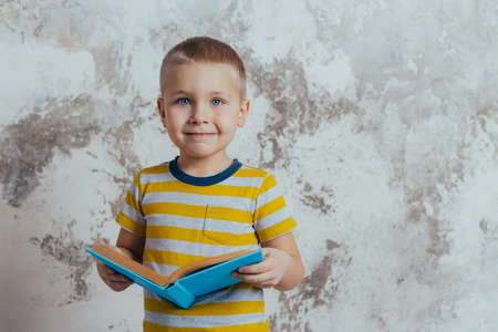 Little boy posing in front of a gray concrete wall. Portrait of a smiling child wearing a yellow...