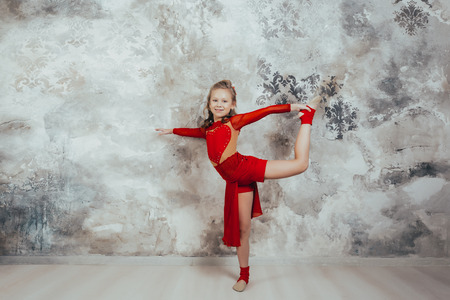 Girl gymnast in a red gymnastic swimsuit posing on studio background. practicing gymnasticの写真素材