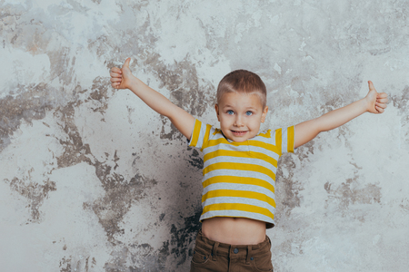 Young boy child in a yellow striped T-shirt celebrating a happy smiling laugh with a hand spread over a gray backgroundの写真素材