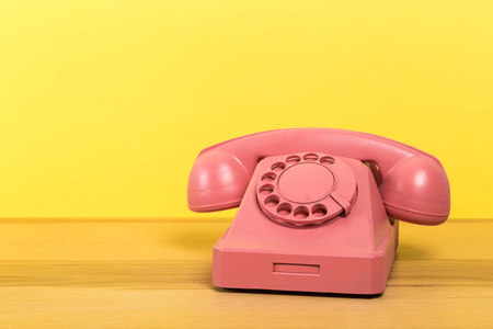 Vintage old pink telephone on wooden table with color wall backgroundの写真素材
