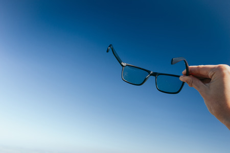 Female hand holding sunglasses against palm tree and blue sunny sky, summer vacation holidays conceptの写真素材