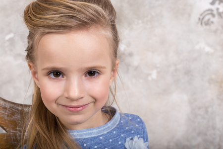 Portrait of a little attractive smiling girl in a blue sweater and pants with hair folded into her hair against a grunge wall background. Studio shot with place for text, fashion conceptの写真素材