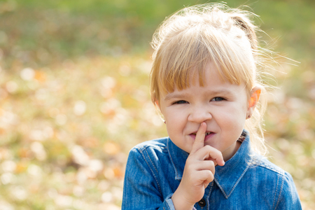 little happy girl in denim sweater put a finger to her lipsの写真素材