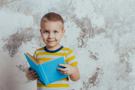 Little boy posing in front of a gray concrete wall. Portrait of a smiling child wearing a yellow striped t-shirtの写真素材