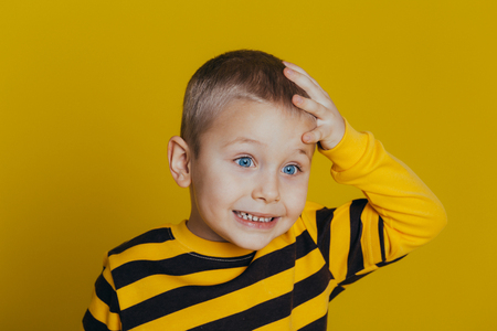 Portrait of an attractive thoughtful boy in a striped sweater holding a hand on his head close-up, on a yellow backgroundの写真素材