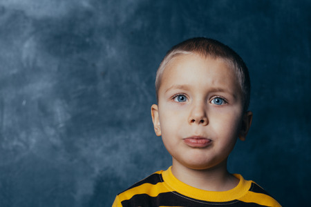 Portrait of an upset cute little child looking at camera against blue concrete wall backgroundの写真素材
