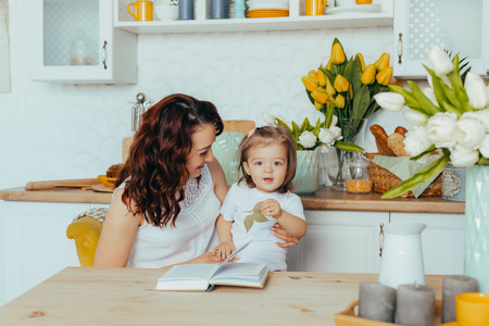 Cute girl and her mom are reading recipes at home in the kitchen.の写真素材