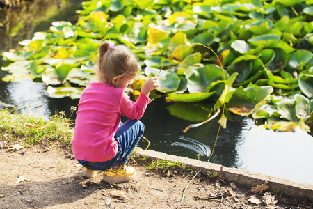 little girl in a pink blouse plays in the park by the pondの写真素材