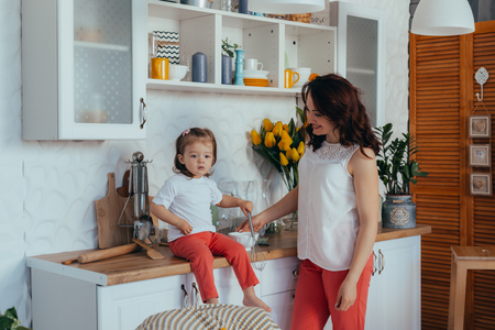 Beautiful young mother and her cute little daughter play and smile while cooking in the kitchen at home.の写真素材