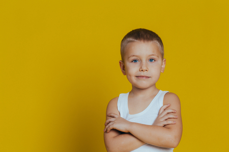 Portrait of an attractive smiling boy in a white T-shirt, arms folded close up, on a yellow backgroundの写真素材