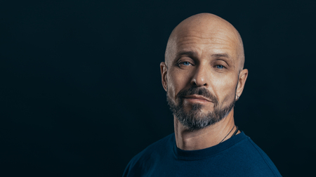 Serious middle aged man with a deadpan face expression dressed in casual posing on a dark gray background with copy spaceの写真素材