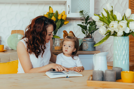 Cute girl and her mom are reading recipes at home in the kitchen.の写真素材