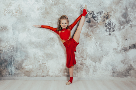 Girl gymnast in a red gymnastic swimsuit posing on studio background. practicing gymnasticの写真素材