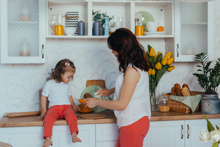 Beautiful young mother and her cute little daughter play and smile while cooking in the kitchen at home.の写真素材