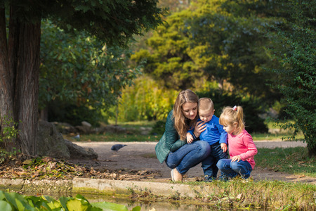 mother plays with her daughter and son in the park by the pond. happy and friendly familyの写真素材
