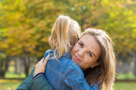 happy mother playing with her daughter hugging her in the park on a summer dayの写真素材
