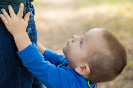 portrait of a little boy wearing a blue jacket touching his mom on a sunny day in the parkの写真素材