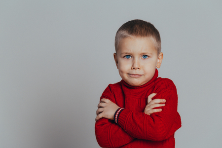 Portrait of attractive serious boy in red sweater with folded hands close up, on gray backgroundの写真素材