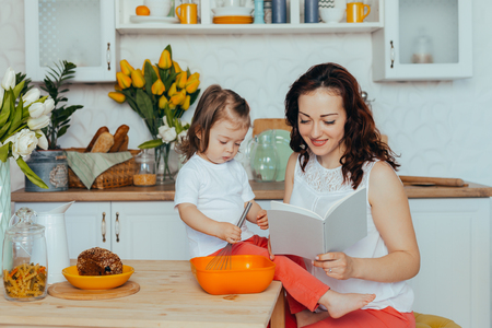 Beautiful young mother and her cute little daughter play and smile while cooking in the kitchen at home.の写真素材