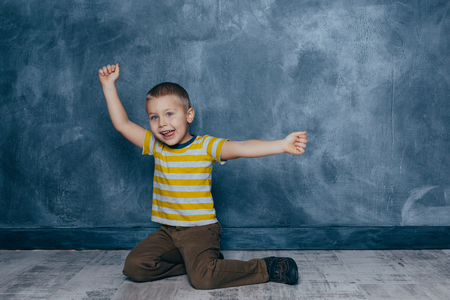 A young emotional boy sits on a wooden floor against the background of a blue wall in the studio. Human emotions, facial expression concept.の写真素材