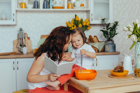 Beautiful young mother and her cute little daughter play and smile while cooking in the kitchen at home.の写真素材