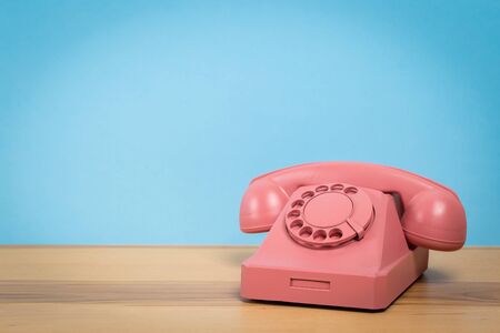 Vintage old pink telephone on wooden table with color wall backgroundの写真素材