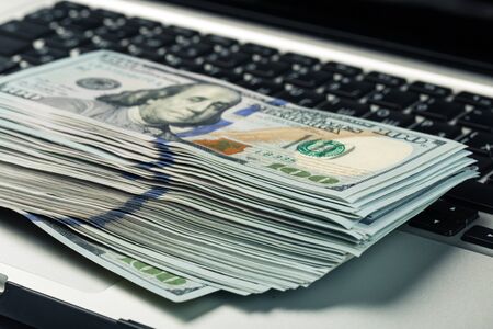 Closeup view of one hundred dollar banknotes lying on the laptop keyboard. Paying dollar for...