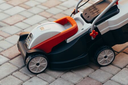 new electric lawn mower on the tile near the garden. toned photoの写真素材