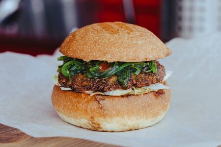 Delicious fresh homemade vegetarian cheese burger with chuka salad, cheese, tomatoes, lettuce and onion rings in kraft paper. street food on wooden backgroundの写真素材