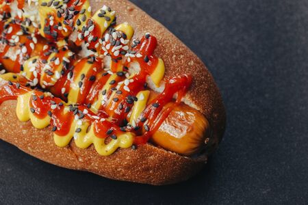 Big hotdog with sausage tomatoes, mustard and salad isolated on black background. Top view.の写真素材