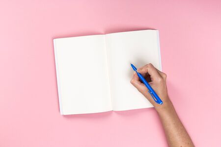 Woman's hands with perfect manicure holding pencil and  notepad as mockup for your design. Pink background, flat layの写真素材