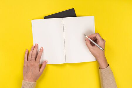 Woman's hands with perfect manicure holding pencil and  notepad as mockup for your design. Yellow background, flat layの写真素材
