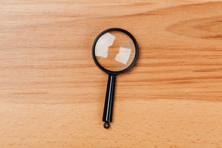 Small magnifying glass on wooden table, search